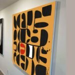 Large-scale yellow modernist abstract painting with crisp black-and-white shapes, shown at an angle to reveal the painting’s edges and depth.